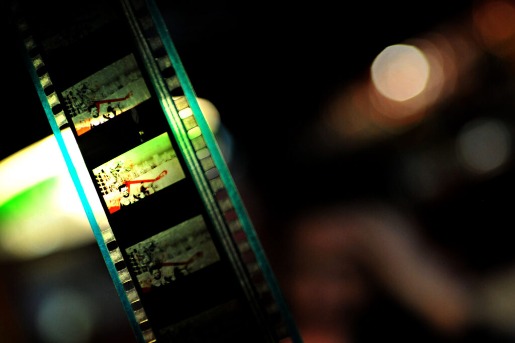 Filmstreifen im Gegenlicht mit mehreren Einzelbildern und Perforation, im Hintergrund unscharfe Lichter