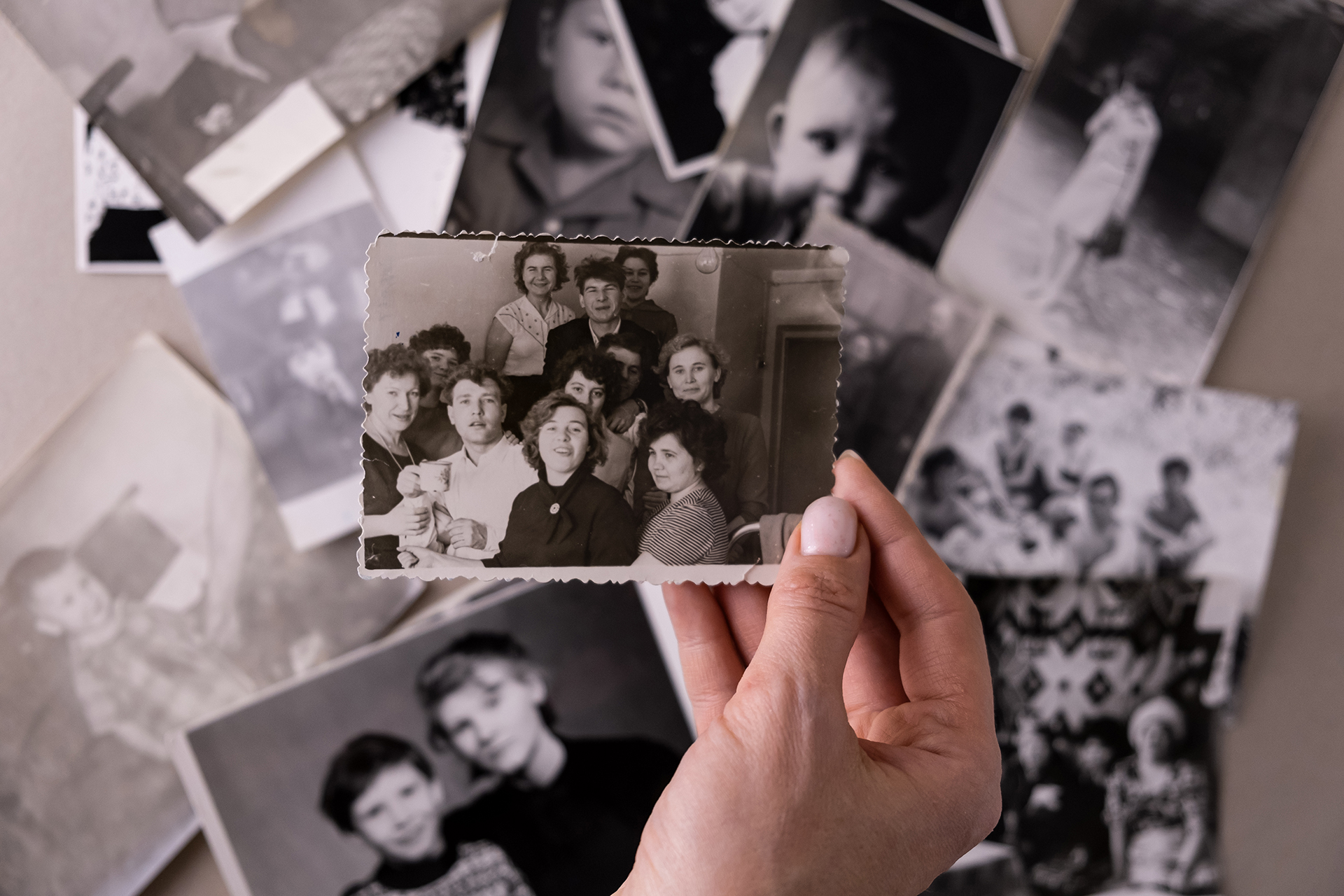 Hand hält ein altes Schwarz-Weiß-Foto einer Gruppe von Kolleginnen und Kollegen, im Hintergrund weitere historische Fotos auf einem Tisch